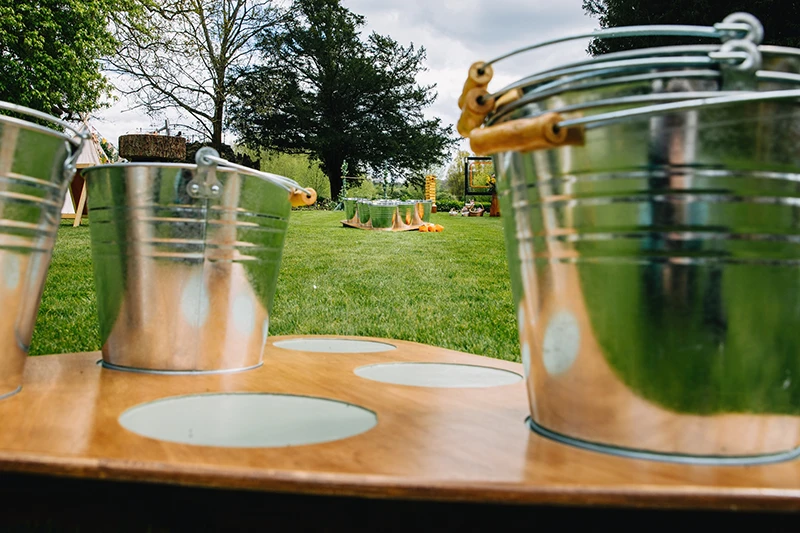 Close-up of Bucket and Ball garden game, showing metal buckets with wooden handles on a wooden platform, by Thistle & Rose Events.