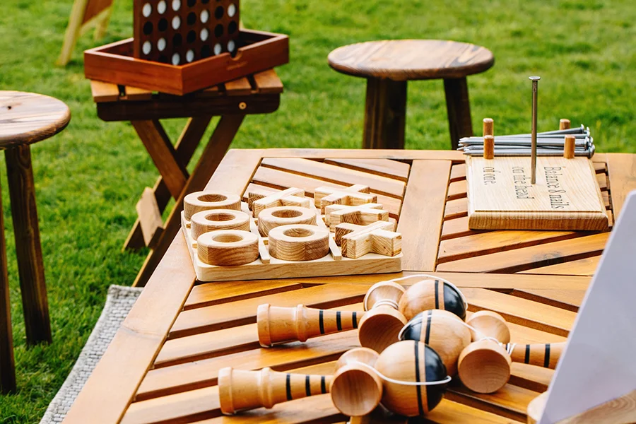 Wooden garden games on a wooden table, including Noughts and Crosses, Balance the Nail game, and a handle-and-ball game, by Thistle & Rose Events.