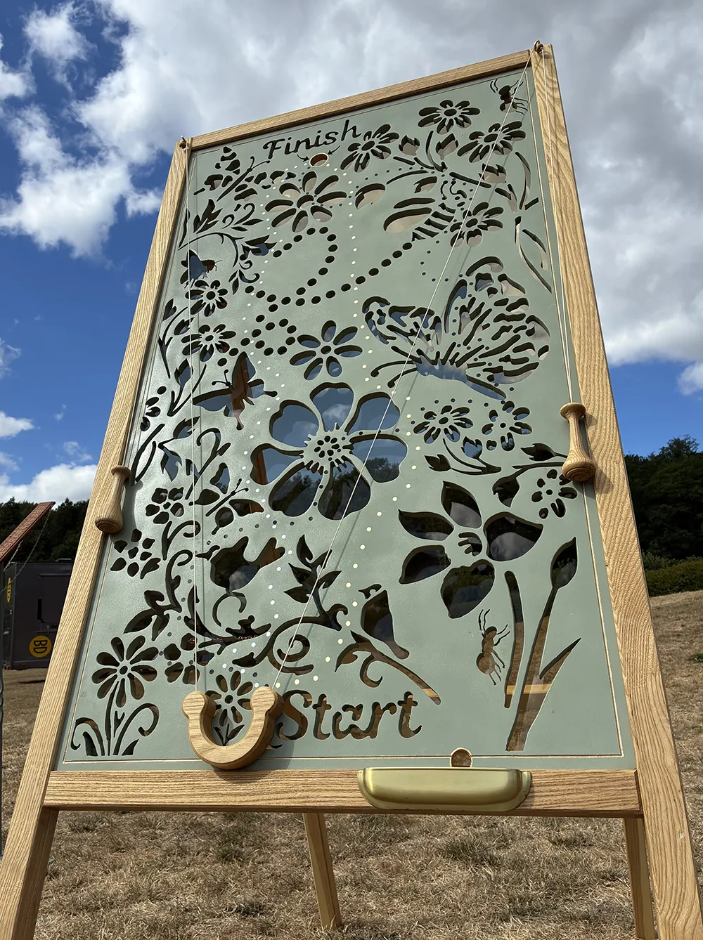 Bottom-up view of the handcrafted Maze Wall garden game with blue sky and clouds above, by Thistle & Rose Events.